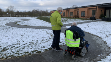 En person i kørestol ledsages af en gående person udenfor