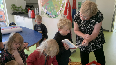 Voksne og børn kigger i bøger i en daginstitution.