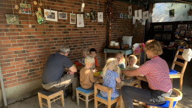 Børn og voksne sidder ved et bord hos to dagplejere