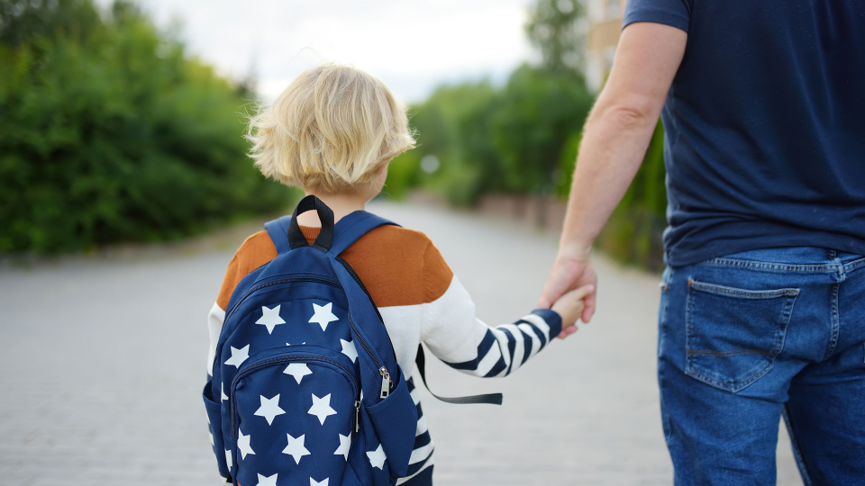 Barn med skoletaske holder i hånd med voksen