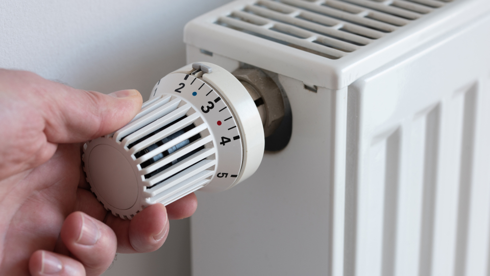 Billedet viser en hånd der regulerer på en radiatortermostat